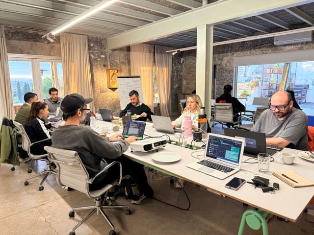 A team working with laptops around a table at a HeyBeta workshop.